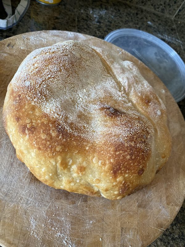 A floured, blistered round loaf cooling on a wooden board