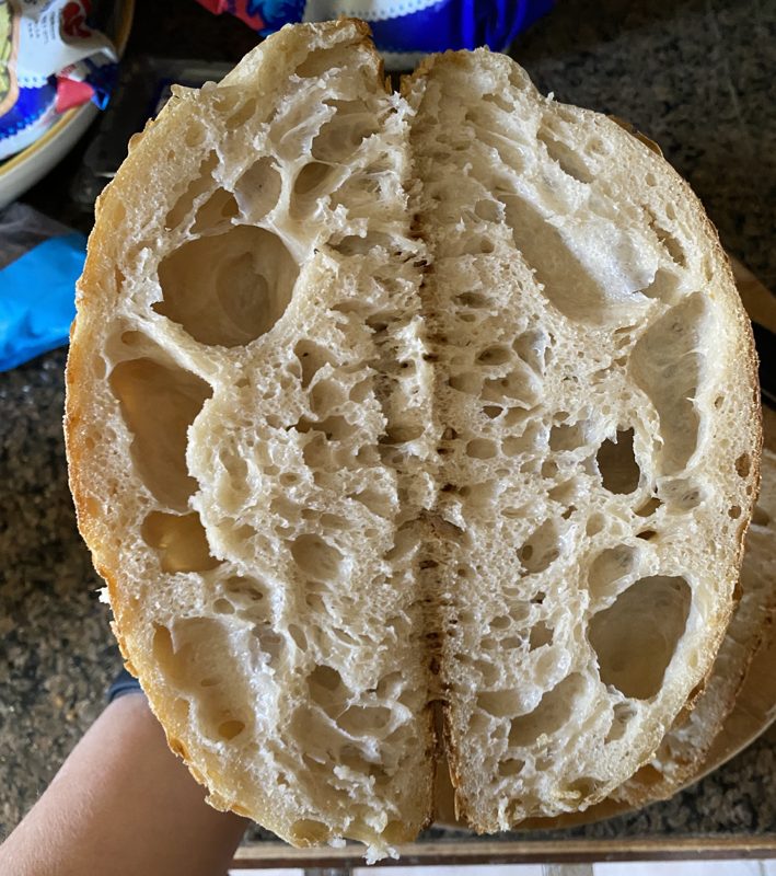 A round sourdough loaf cut in half, held open to show a wide, airy crumb full of large holes